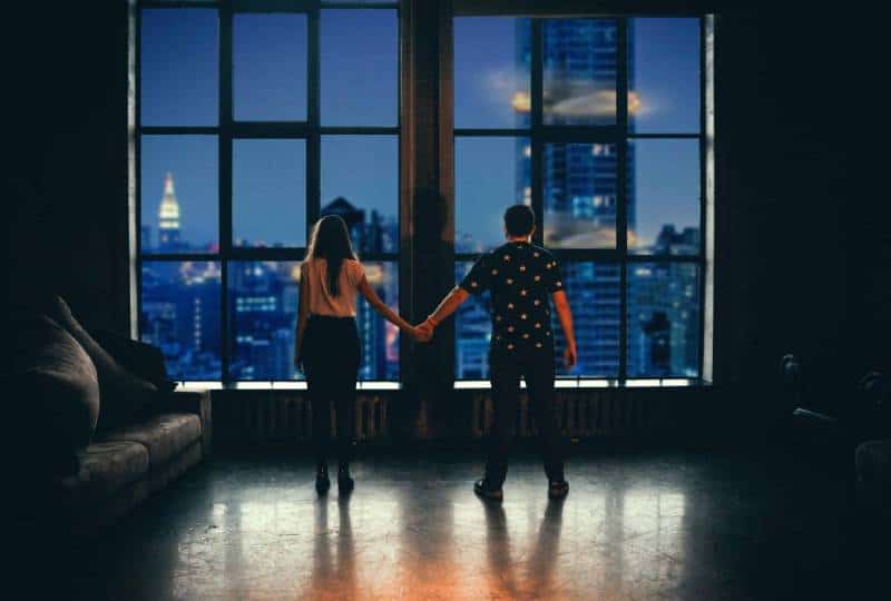 un homme et une femme sont debout près de la fenêtre se tenant la main