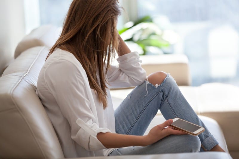 une femme assise sur un canapé tient un smartphone