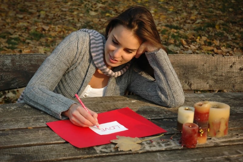 une femme heureuse assise à une table en bois et écrivant une lettre d'amour
