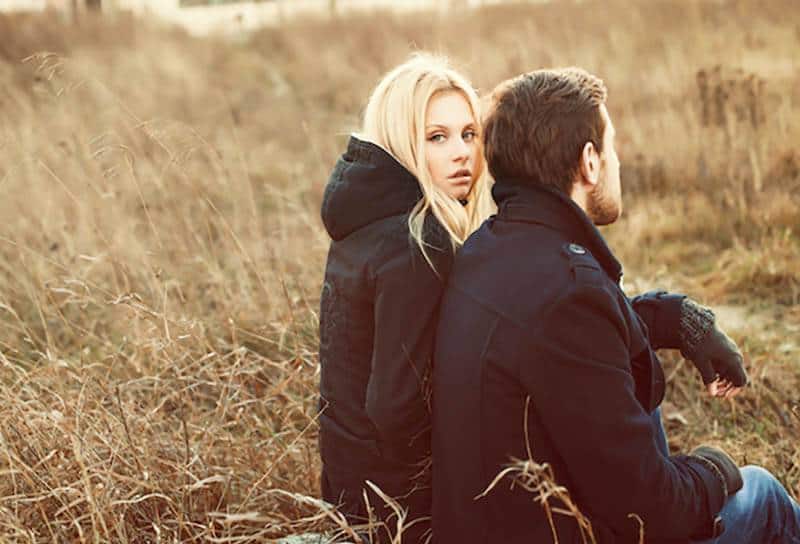 une femme blonde attentionnée assise à côté d'un homme portant une veste noire et des gants à l'extérieur