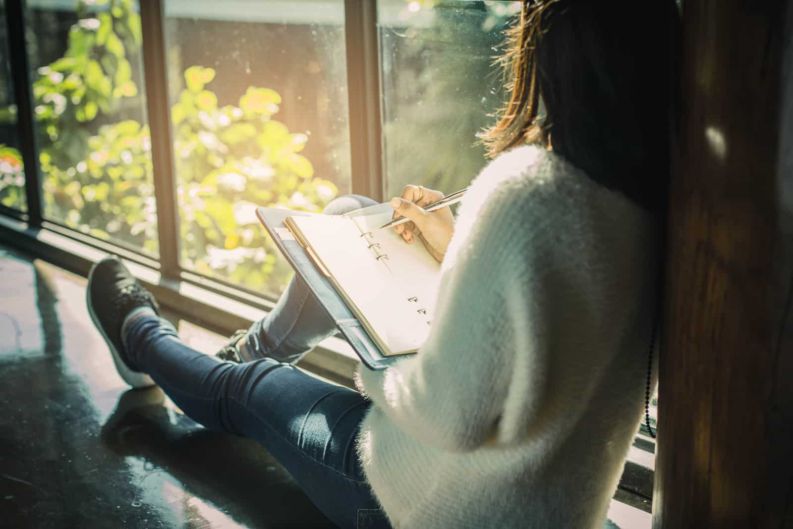 une femme est assise près de la fenêtre et écrit