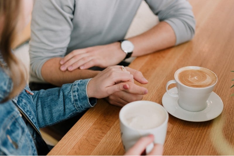 Une femme touchant les mains de l'homme assis à une table côte à côte avec des tasses à café sur la table