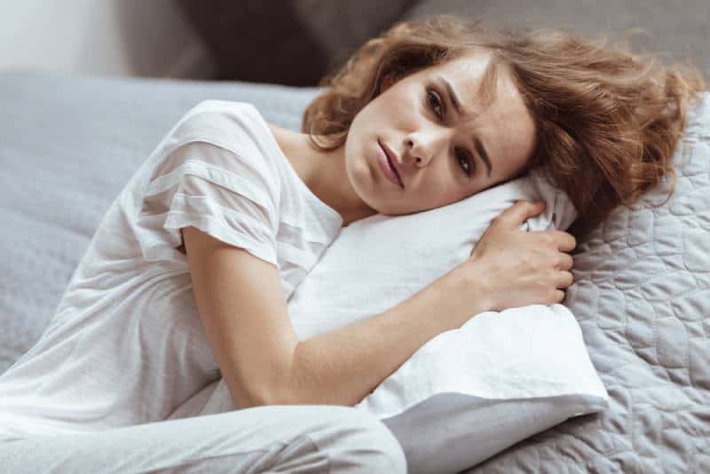 Femme inquiète, allongée sur un oreiller, pensant à quelque chose de déprimant à la maison.