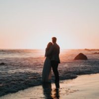 photo de silhouette d'un couple se tenant sur la plage et regardant le coucher de soleil