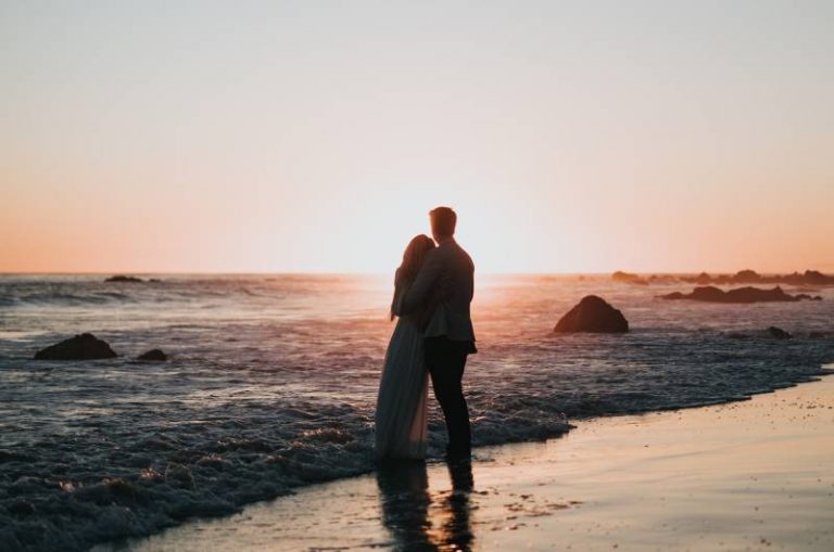 photo de silhouette d'un couple se tenant sur la plage et regardant le coucher de soleil