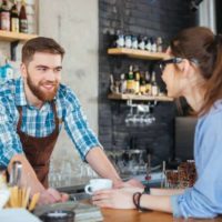Barista souriante et jeune jolie femme à lunettes discutant dans un café