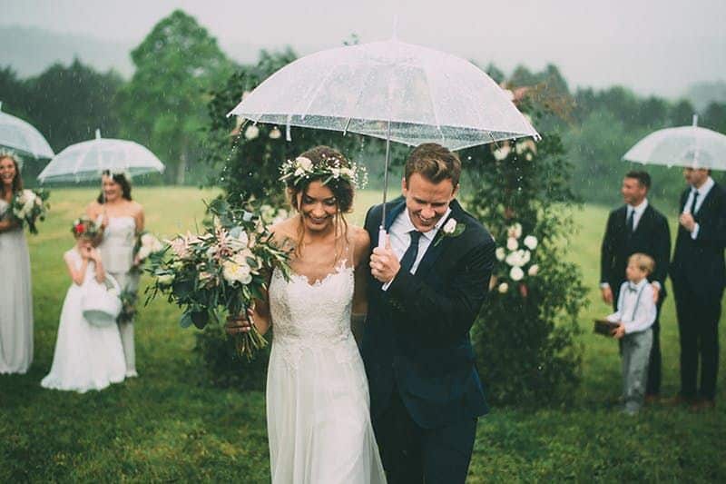 Le marié et la mariée sous un parapluie pendant le désherbage sous la pluie