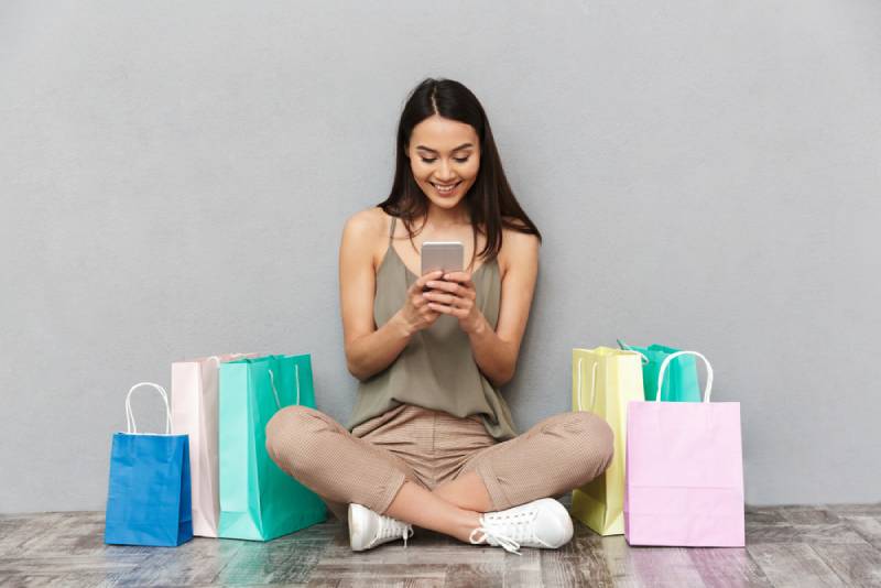 Portrait d'une femme asiatique souriante, assise et tenant son téléphone portable