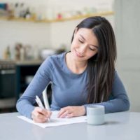 Une femme souriante écrit une lettre à la maison