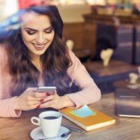 Une femme souriante envoie des SMS sur son téléphone au café