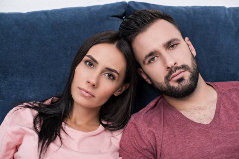 Un jeune couple sans émotion, appuyé l'un contre l'autre alors qu'il est assis sur le canapé