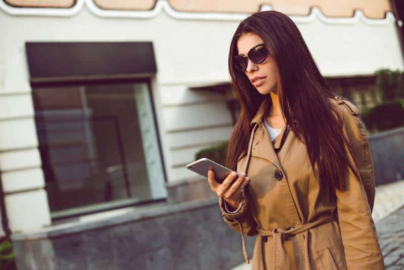 Une belle jeune femme dans une tranchée utilise son téléphone portable
