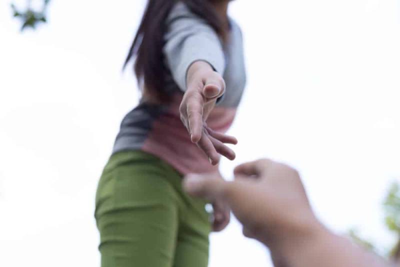 Une femme en pantalon vert offre à un homme un coup de main pour se lever