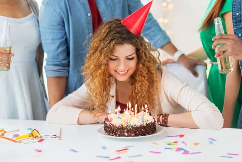 Une femme rousse heureuse et souriante avec des bougies allumées sur un gâteau d'anniversaire lors d'une fête à la maison