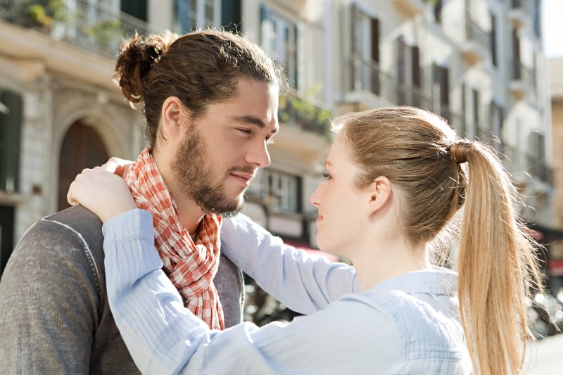 Vue de côté d'un couple souriant qui s'embrasse et se regarde à l'extérieur