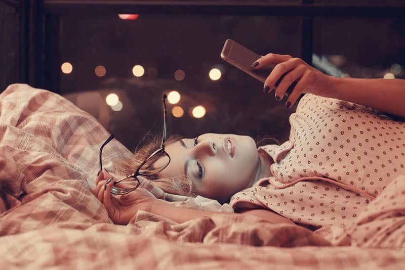 belle jeune femme allongée sur le lit et regardant son téléphone