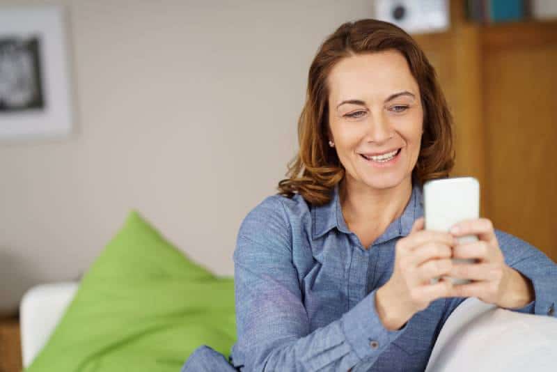 femme d'âge moyen se détendant à la maison sur le canapé en lisant ses SMS