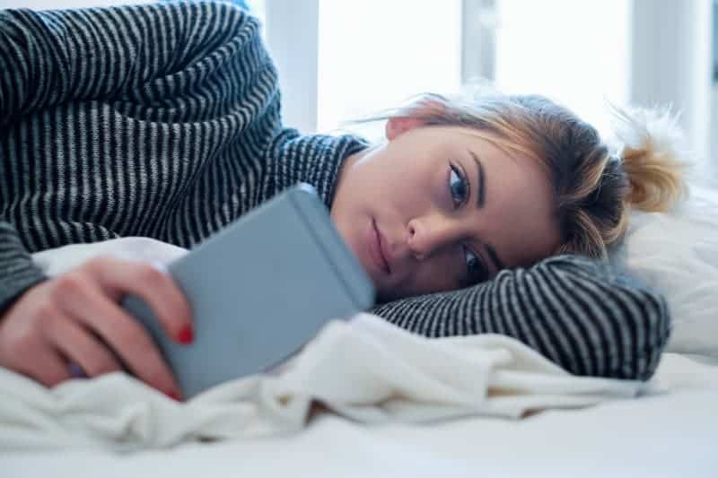 femme réfléchie, allongée sur son lit et tapant sur son téléphone