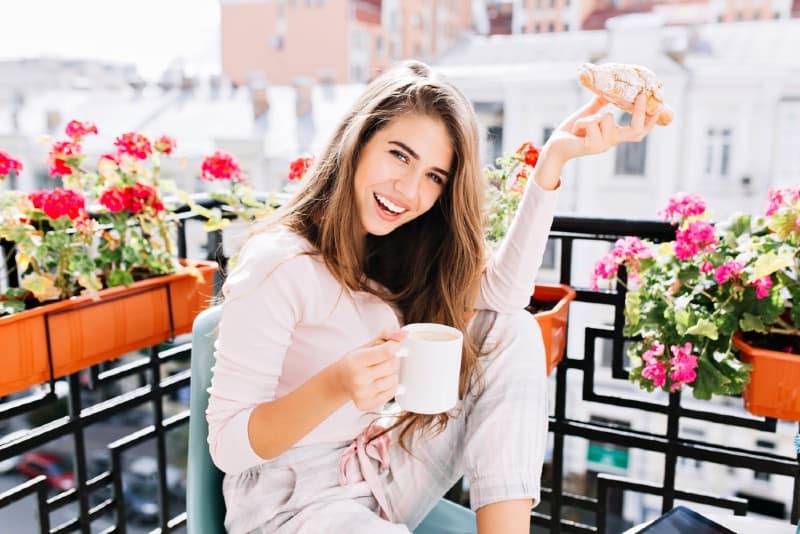 Portrait belle fille aux cheveux longs prenant son petit déjeuner sur le balcon entourent les fleurs le matin en ville.