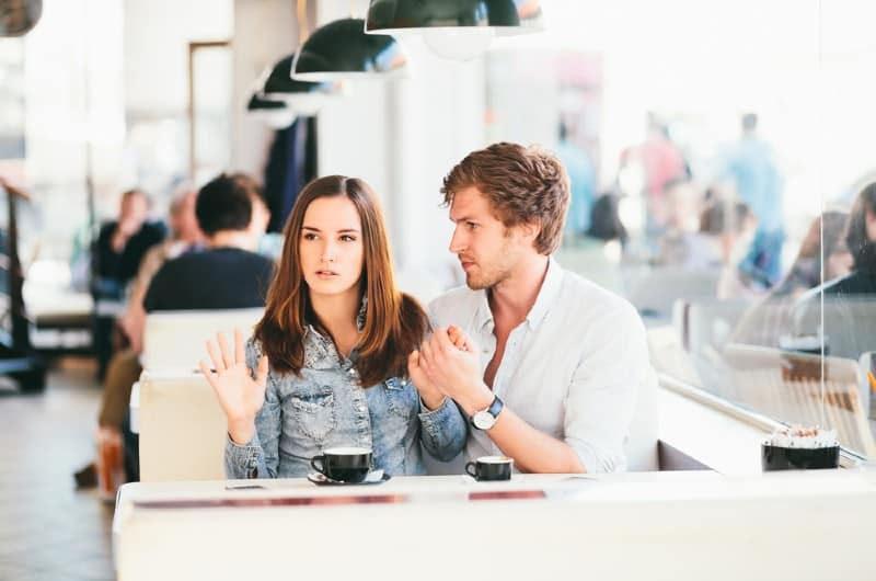Jeune couple se battre dans un café assis à une table côte à côte