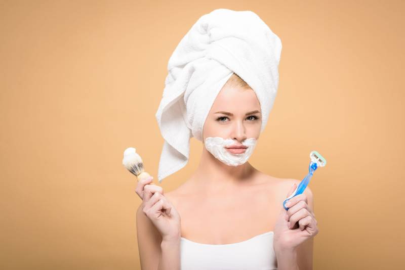 jeune femme avec une serviette sur la tête et de la crème à raser