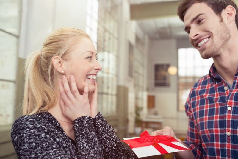 Beau mari souriant donnant à sa jolie jeune femme blonde une carte surprise
