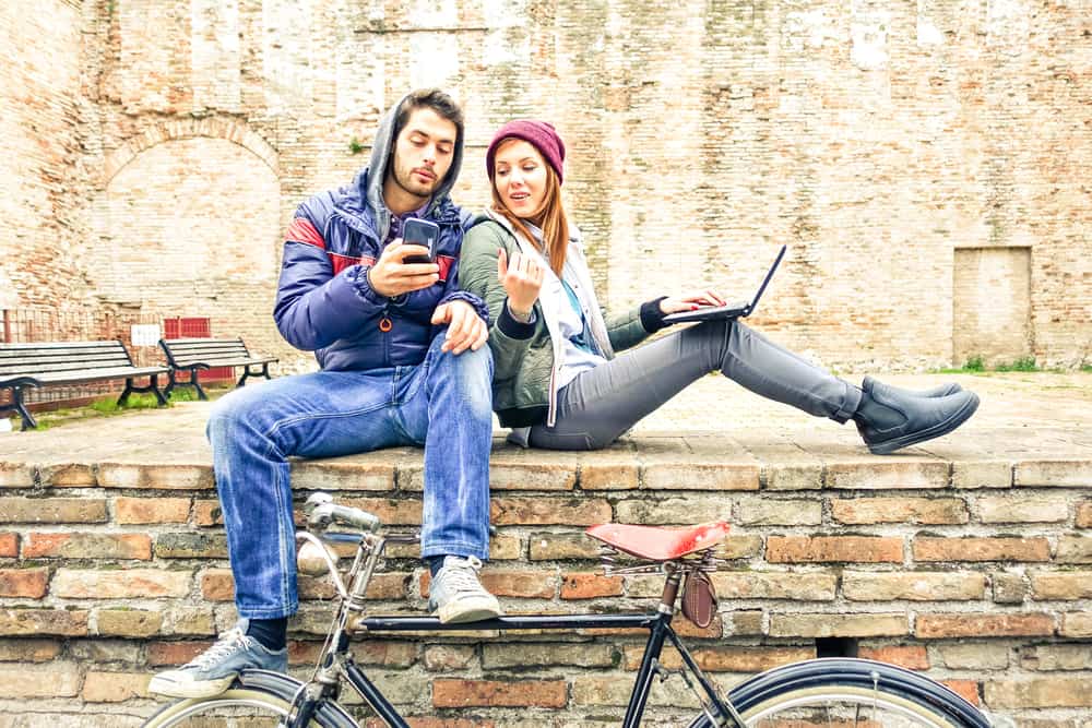 un homme et une femme assis à l'arrière, il tient le téléphone dans sa main alors qu'elle est assise derrière l'ordinateur portable