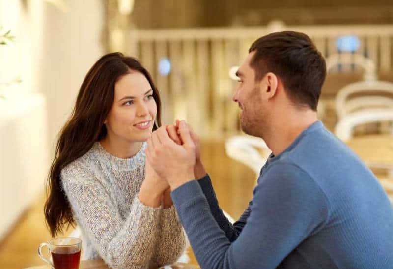 un homme et une femme sont assis à une table pendant qu'il la tient par les bras