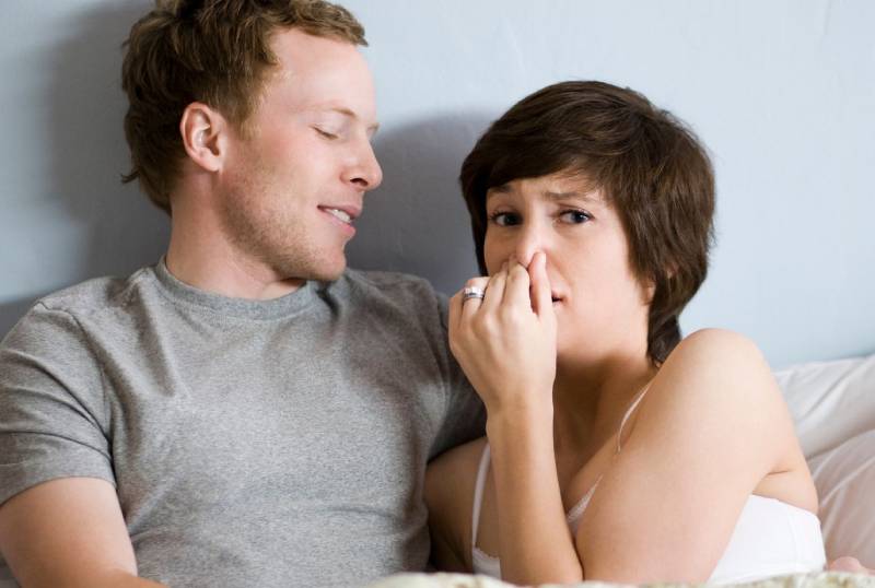 une femme se tient le nez à côté de son petit ami au lit