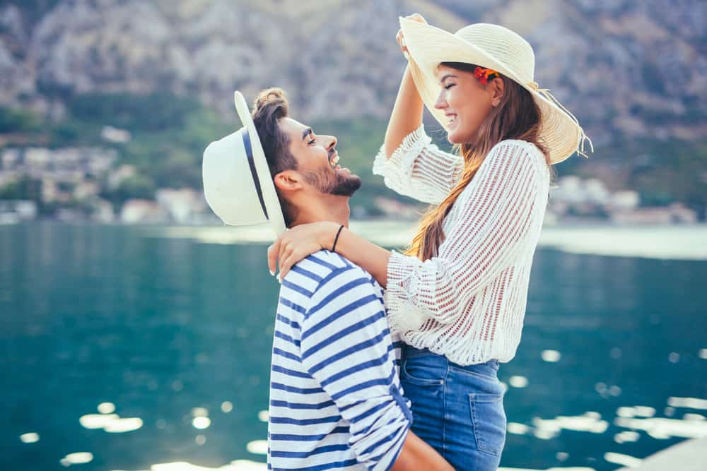 une femme étreint un homme sur une jetée au bord de la rivière avec des chapeaux sur la tête