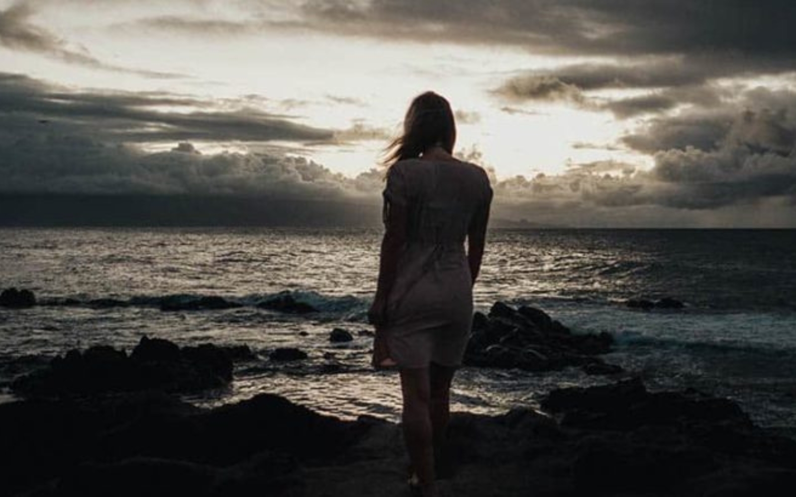 une femme debout au bord de la mer, le dos tourne