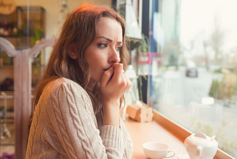 Femme nerveuse assise au café et se ronger les ongles