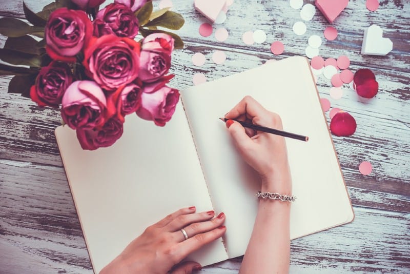 Mains féminines écrivant en cahier ouvert et bouquet de roses sur la vieille table en bois