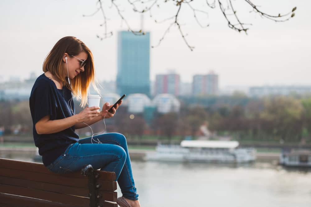 Une femme avec un casque dans ses oreilles est assise sur un banc et tient un téléphone dans sa main