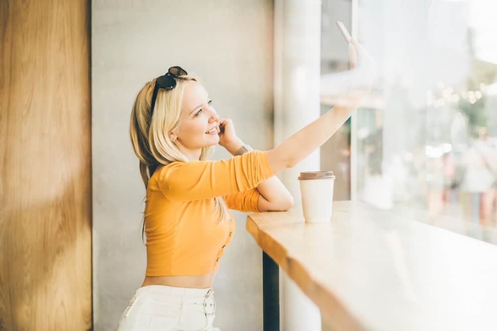 Une femme blonde est assise en train de boire du café et prend une photo