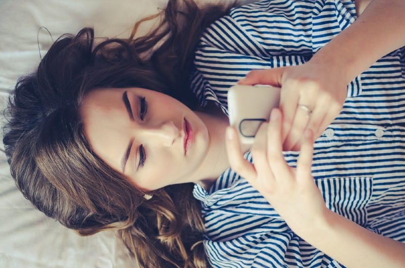 Gros plan d'une adolescente triste couchée dans son lit à l'aide de son mobile