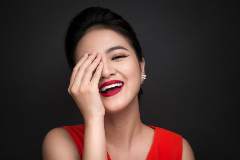 Femme timide souriante ferma son visage avec une main sur fond noir