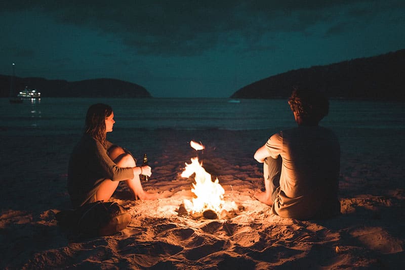 couple assis sur la plage près du feu