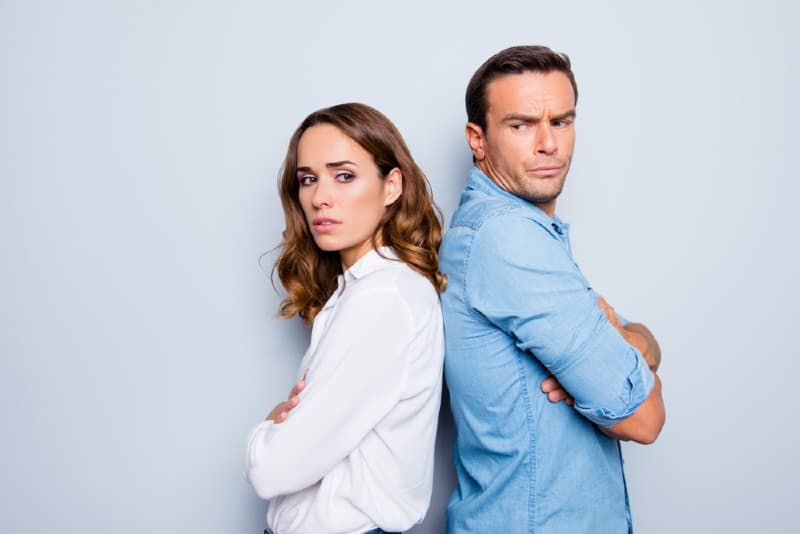 Couple triste debout dos à dos avec les bras croisés en ignorant les uns les autres sur fond gris