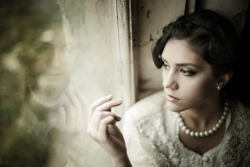 Superbe femme brune aux yeux bruns portant des perles regardant par la fenêtre