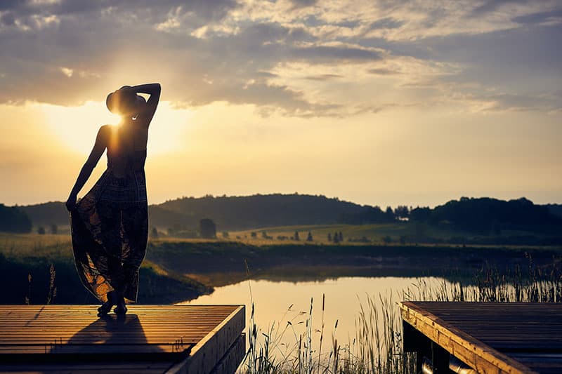 femme debout au bord du lac au coucher du soleil