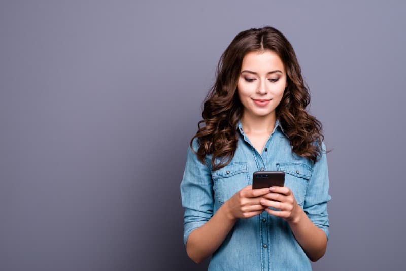 Femme heureuse en chemise en jean décontractée textos sur son smartphone