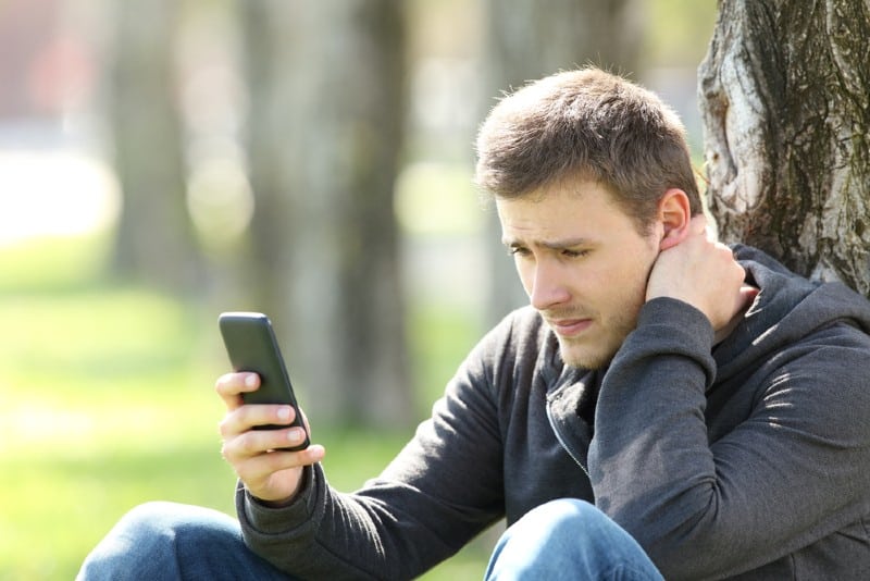 Seul homme triste écrit des messages téléphoniques assis sur l'herbe à l'extérieur dans un parc
