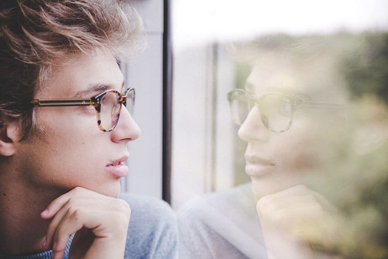 jeune homme avec des lunettes regardant par la fenêtre