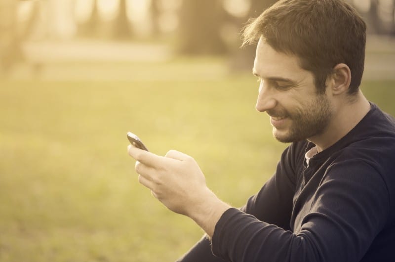 Jeune homme assis dans le parc et envoyer un message sur son téléphone