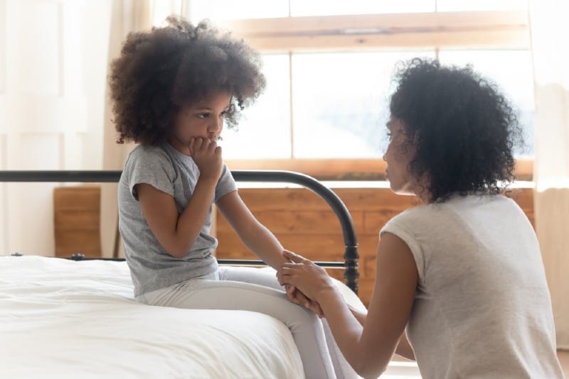Inquiet mère afro-américaine tenant la main de triste petite fille assise sur le lit