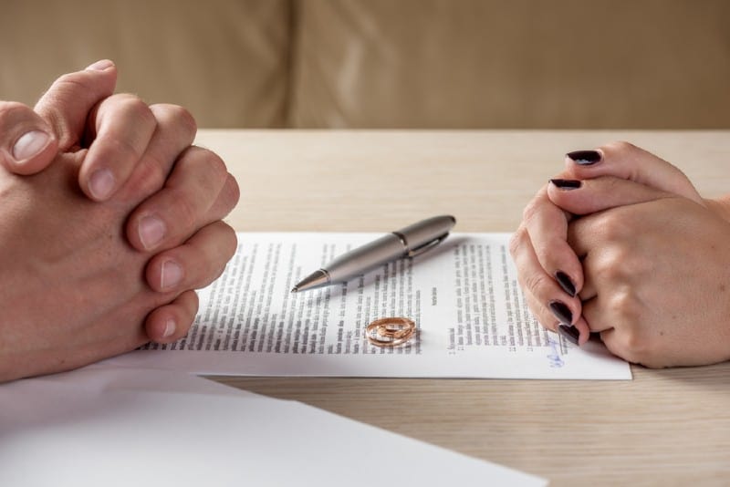 Mains de femme et mari signature des papiers de divorce avec des alliances sur la table