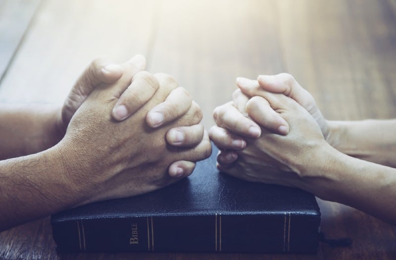 Mains d'homme et femme priant ensemble sur la sainte bible sur table en bois