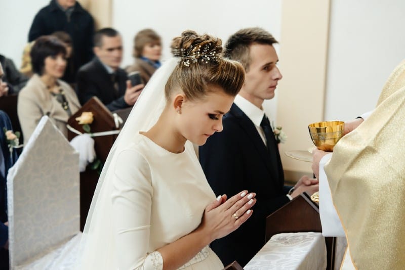 Mariée et le marié priant avec prêtre à genoux lors de la cérémonie de mariage à l'église