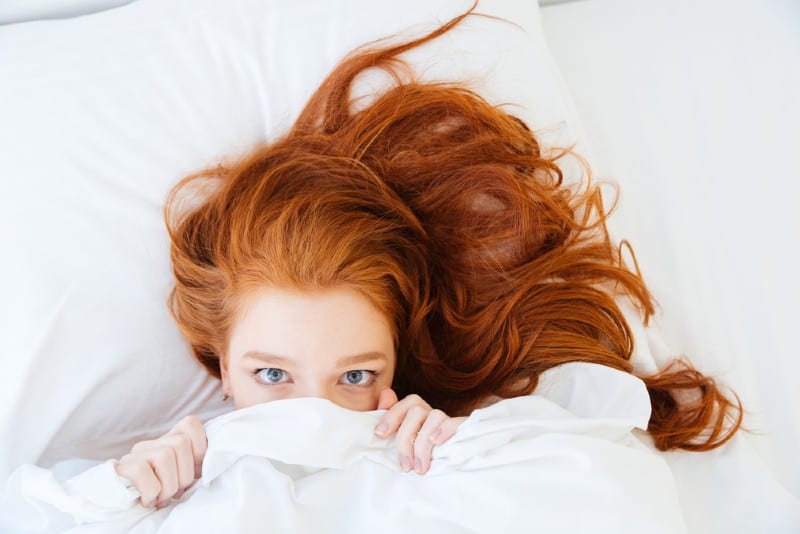 rousse jeune femme couchée dans son lit et se cachant sous le drap